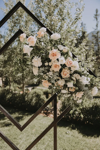 A flower arrangement with blush and white roses are attached to a metal diamond arch.